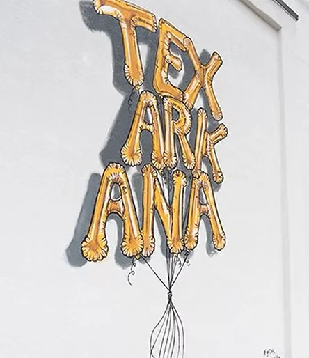 Mural of gold foil balloon letters spelling TEXARKANA on a downtown wall